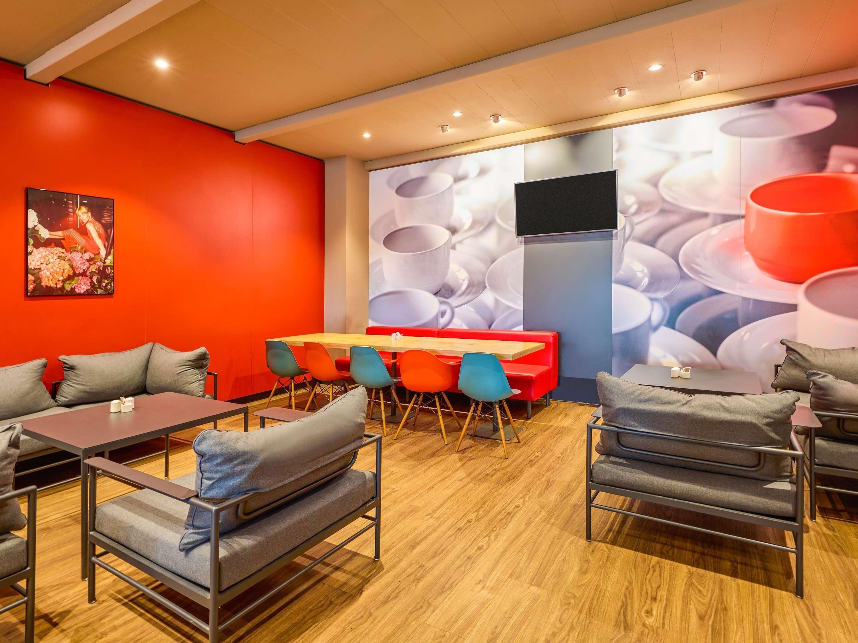 A modern dining area with a red wall, a large mural, and a wooden table with chairs.