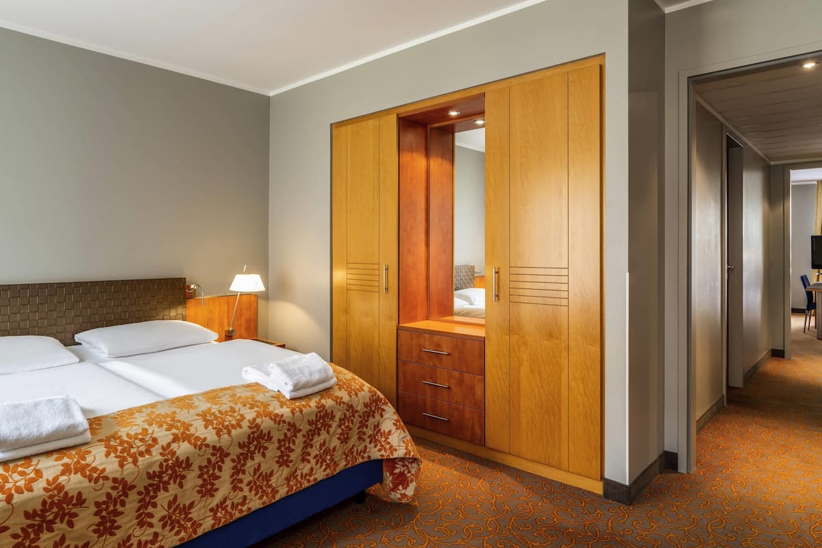 A hotel room with a bed, a wooden wardrobe, a desk, and a chair.