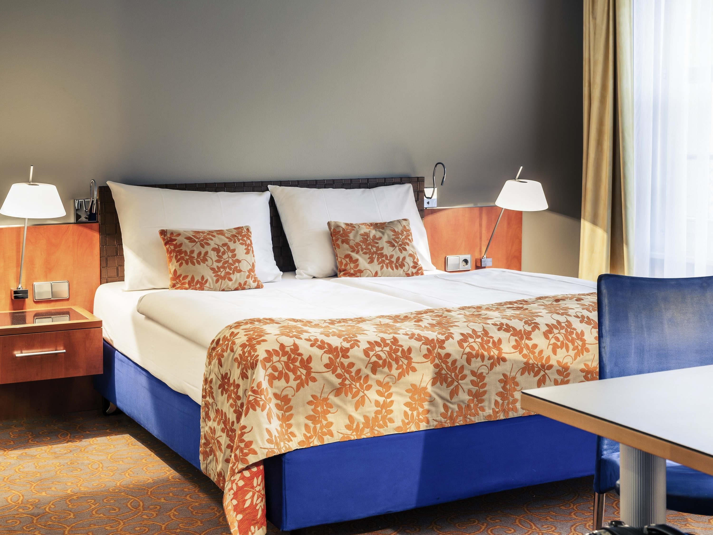 A hotel room with a bed, two bedside tables with lamps, a desk, and a chair.