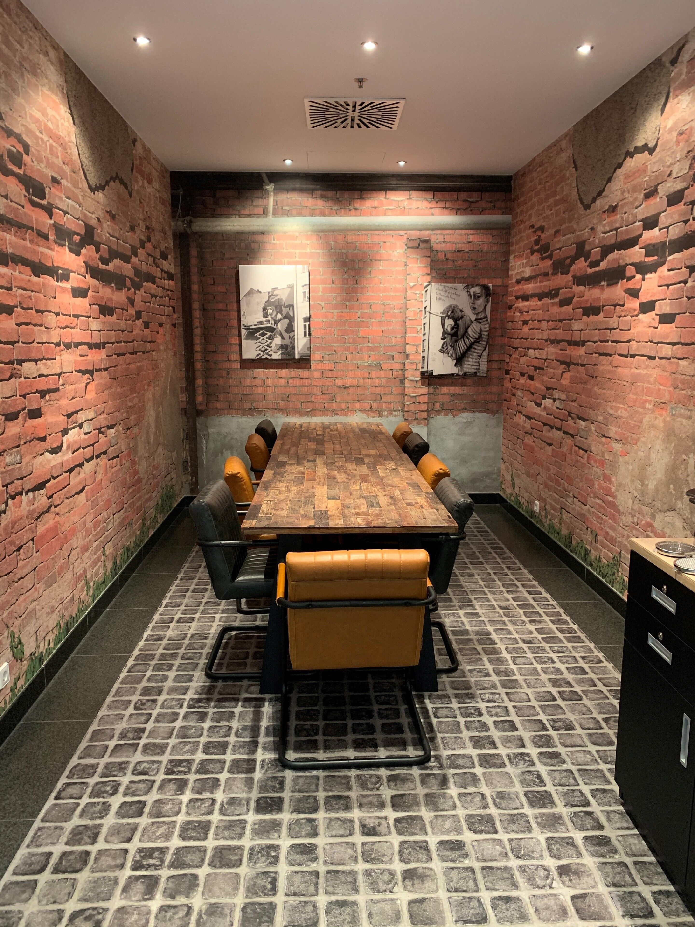 A conference room with a brick wall, a long wooden table, leather chairs, and a patterned floor.