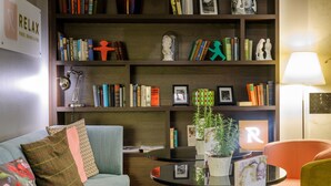 A cozy living room with a bookshelf, a sofa, a coffee table, and a lamp. - Mercure Hotel & Residenz Checkpoint Charlie (Berlin)