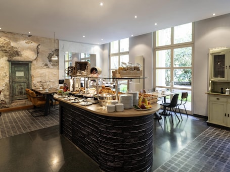 A breakfast bar with various food items, a rustic wall, and large windows.. Mercure Hotel & Residenz Checkpoint Charlie
