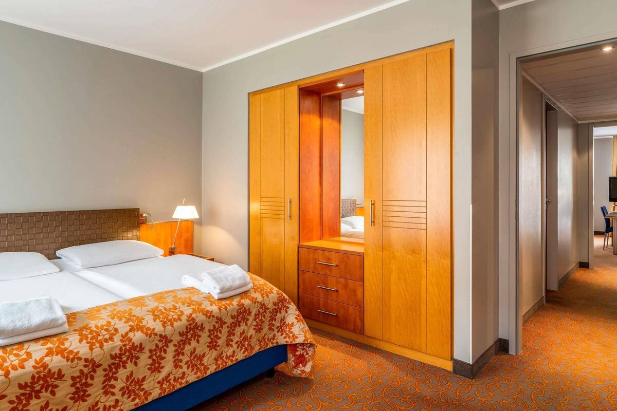 Hotellihuone, jossa on sänky, puinen vaatekaappi, työpöytä ja tuoli.