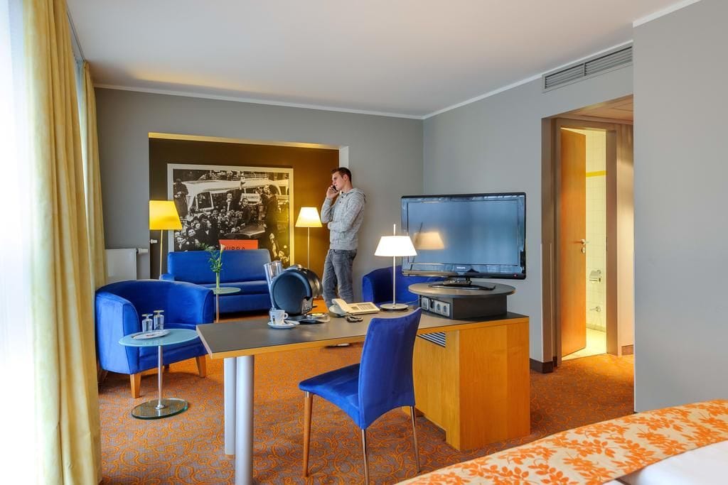Ein Hotelzimmer mit einem Bett, einem Schreibtisch mit Computer, einem Fernseher, einer Couch und einem Couchtisch.