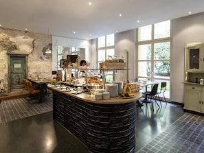 A breakfast bar with various food items, a rustic wall, and large windows. - Mercure Hotel & Residenz Checkpoint Charlie (Berlin)