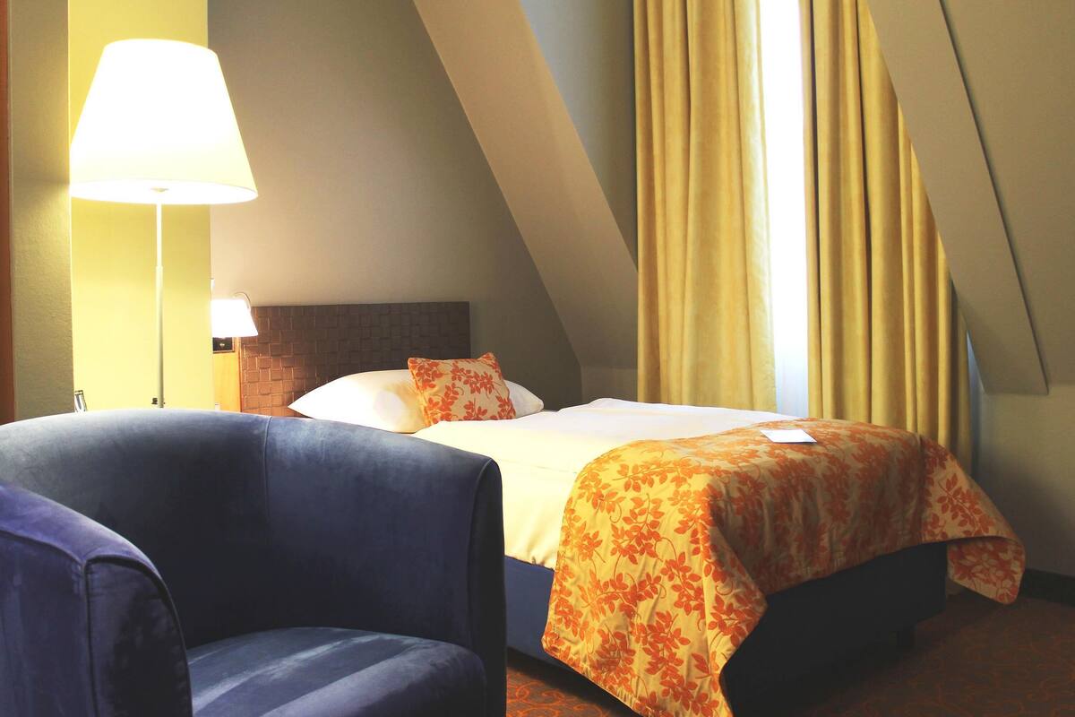 Hotellihuone, jossa on sänky, tuoli, lamppu ja verhot.