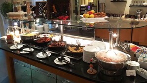 A buffet area with various food items, including fruits, meats, and desserts, displayed on a glass counter. - Mercure Hotel & Residenz Checkpoint Charlie (Berlin)