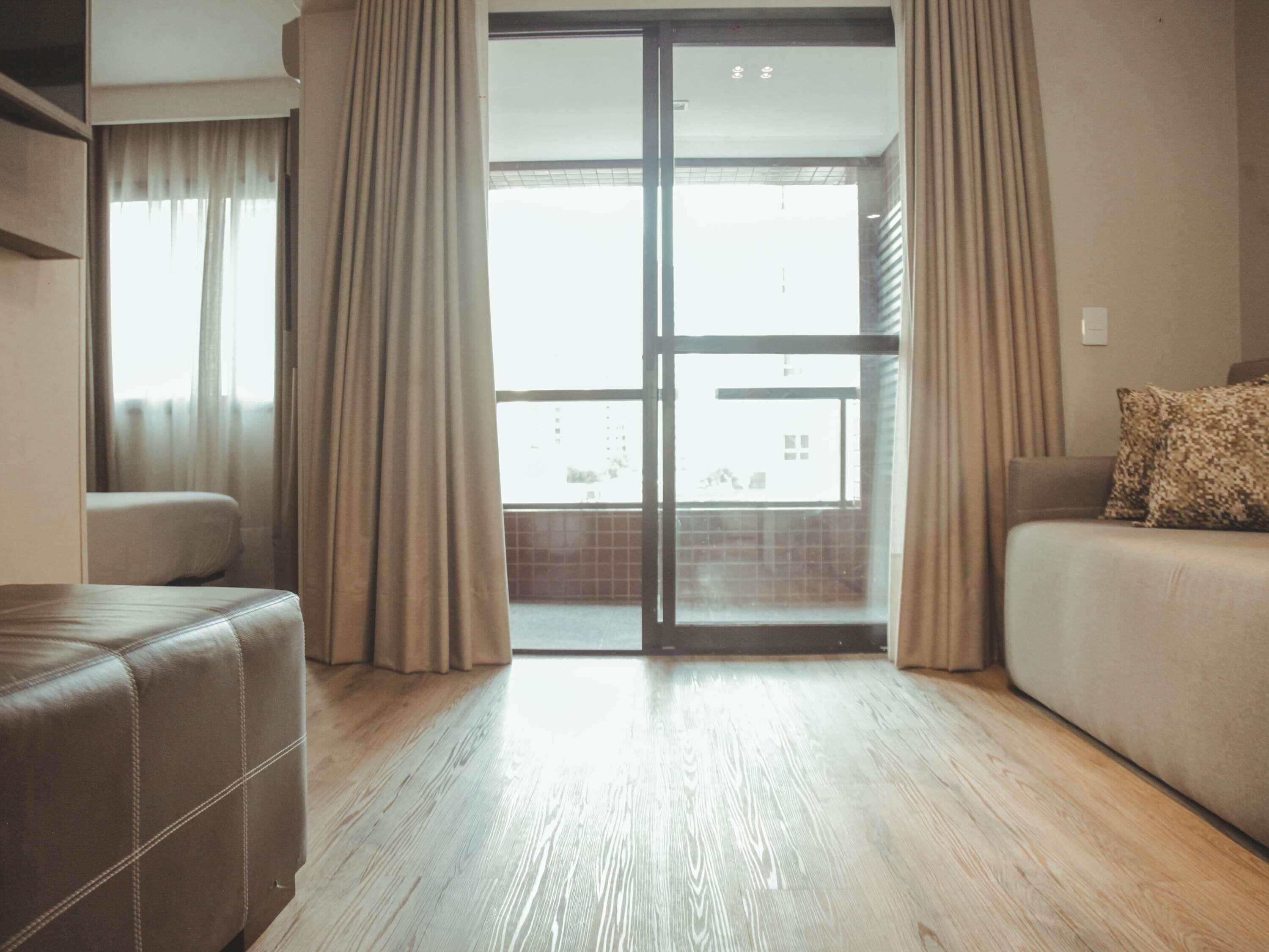A modern living room with a sliding glass door leading to a balcony, a sofa, and a small ottoman.