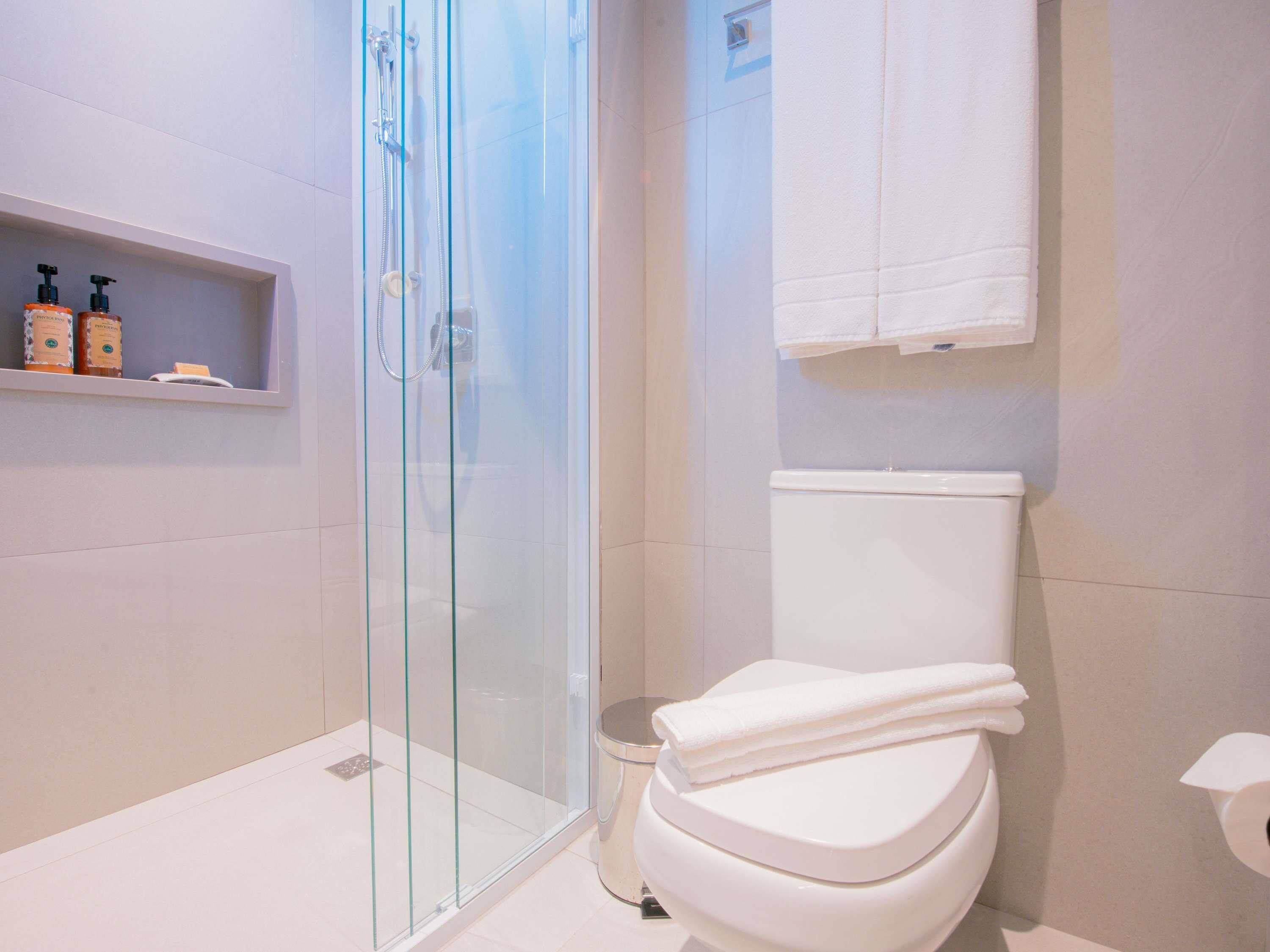 A modern bathroom with a glass shower enclosure, a white toilet, and a shelf with toiletries.