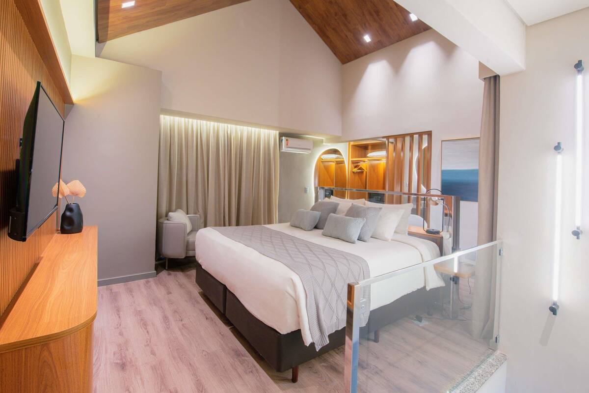 Une chambre moderne avec un grand lit, un plafond en bois, une cloison en verre et un téléviseur fixé au mur.