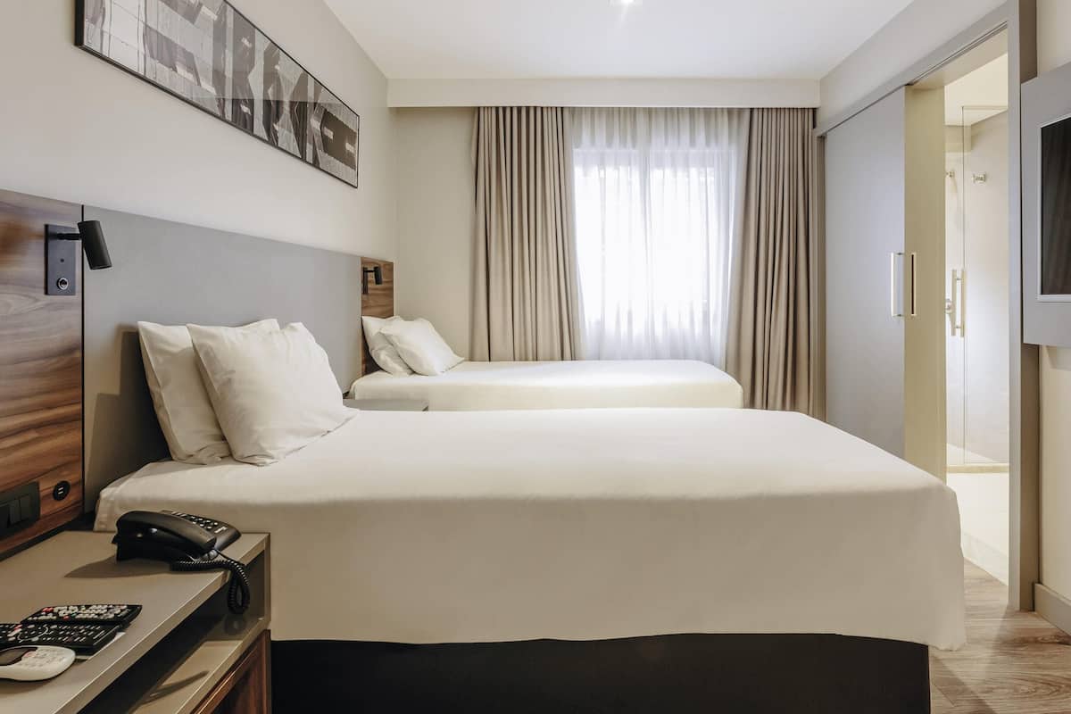 Une chambre d’hôtel avec deux lits, un bureau avec un téléphone, une télévision et un tableau au mur.