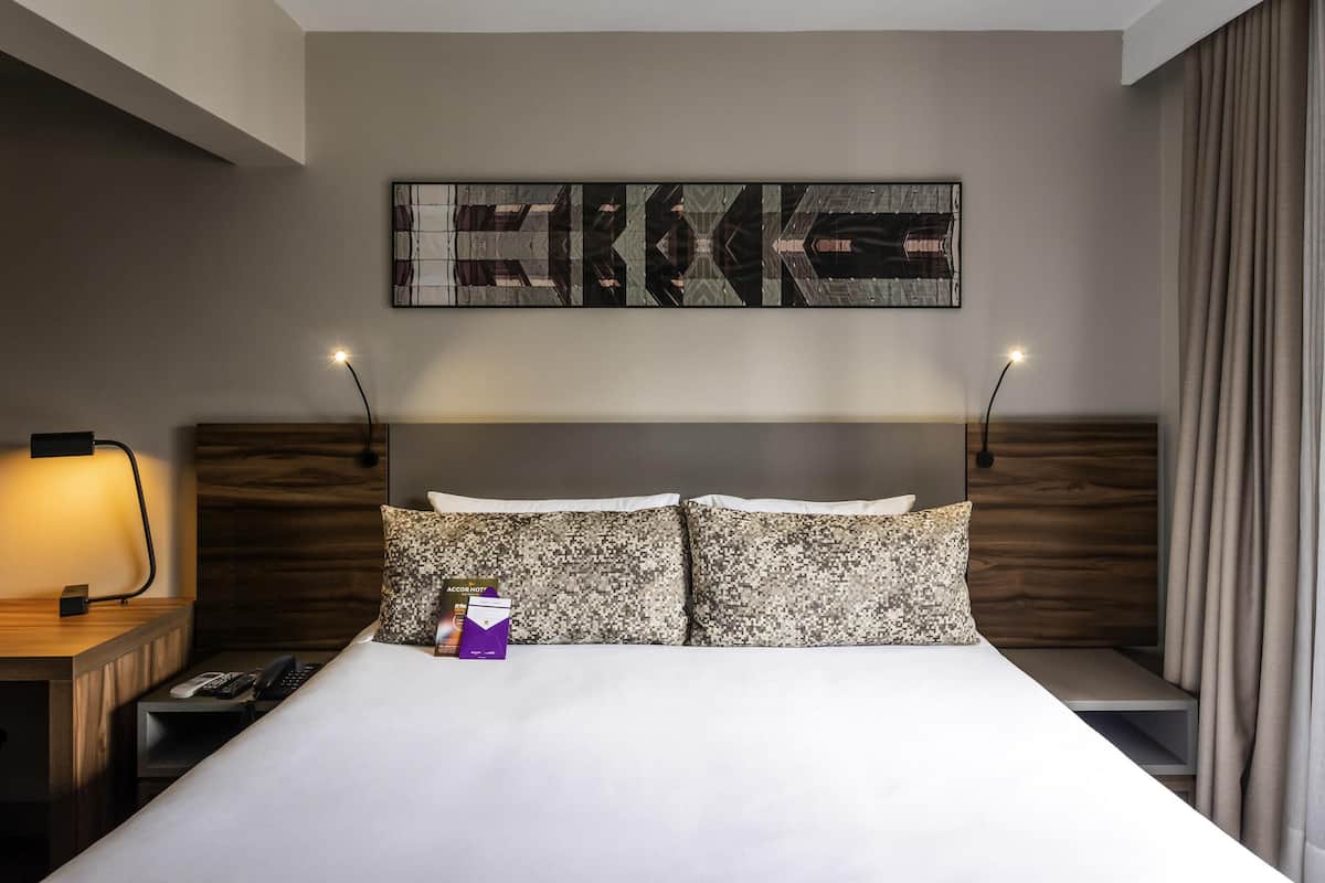 Une chambre d’hôtel avec un grand lit, deux tables de chevet, une petite table, une lampe et une œuvre d’art accrochée au mur.