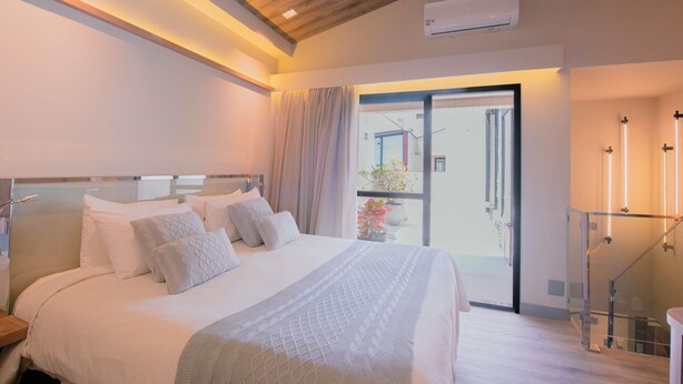 Una habitación de hotel moderna con una cama grande, un ventanal de vidrio que da a un balcón y un techo de madera.
