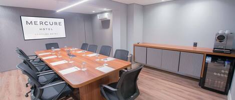 Un salón de conferencias con una larga mesa, sillas, una máquina de café y un equipo de aire acondicionado.
