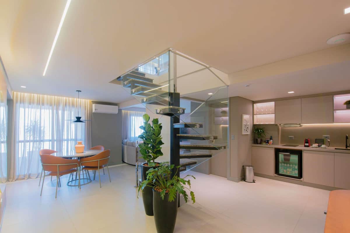 Une cuisine moderne dotée d’un réfrigérateur encastré, un coin repas avec une table ronde et des chaises, et un escalier avec des rampes en verre.