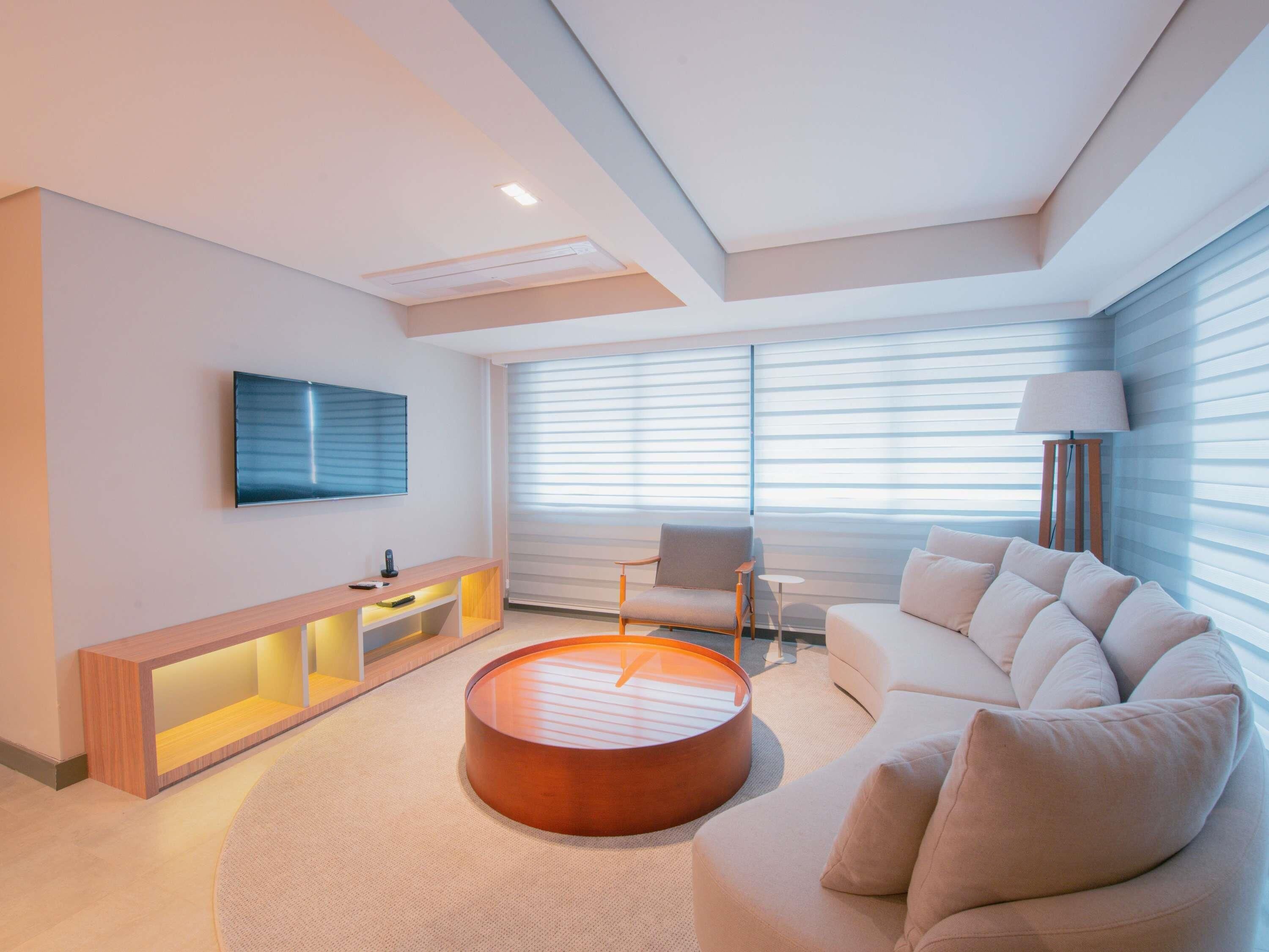 A modern living room with a sofa, a coffee table, a TV, and a window with blinds.