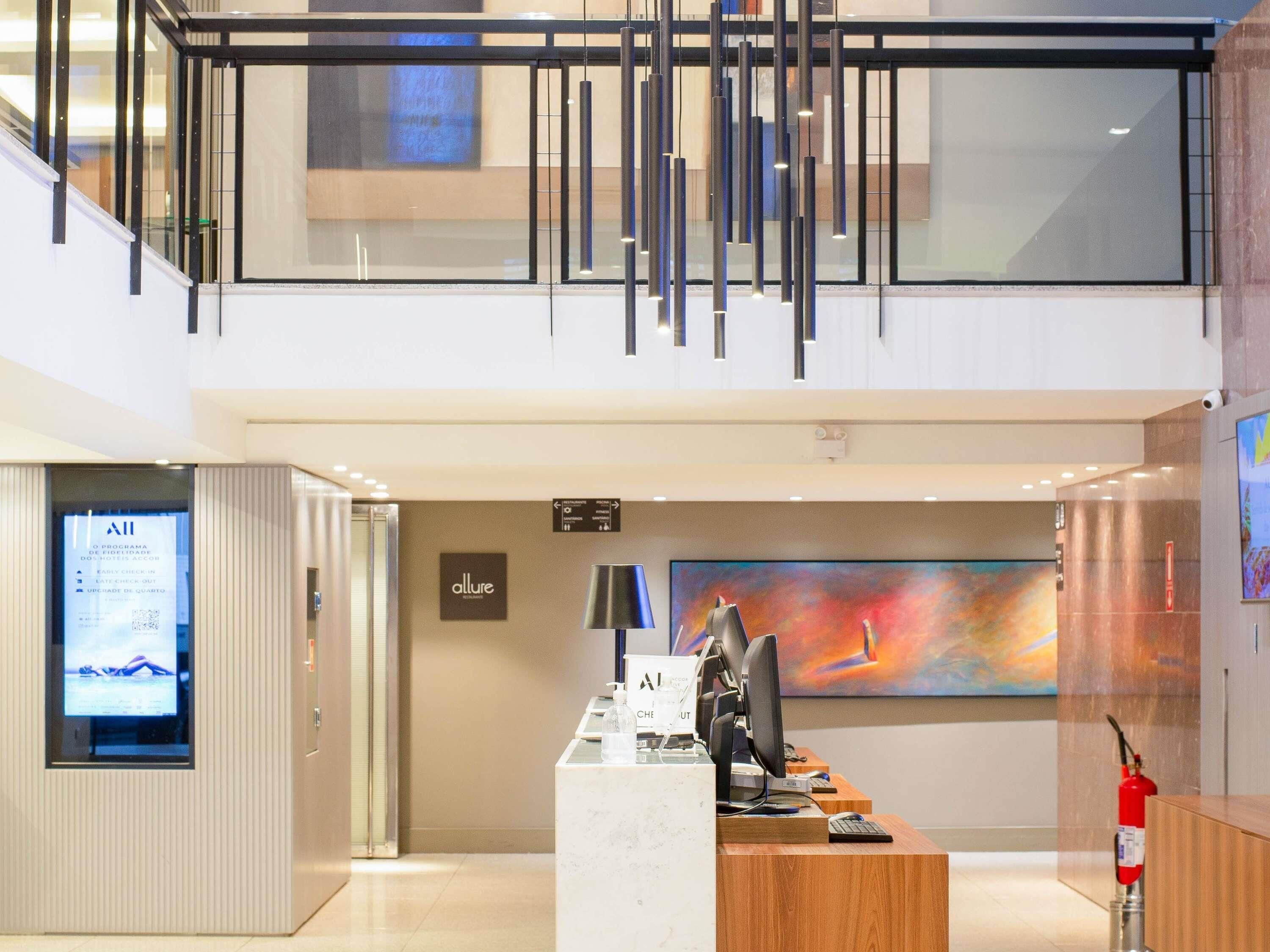 A hotel reception area with a modern design, including a reception desk, a digital screen, and a fire extinguisher.