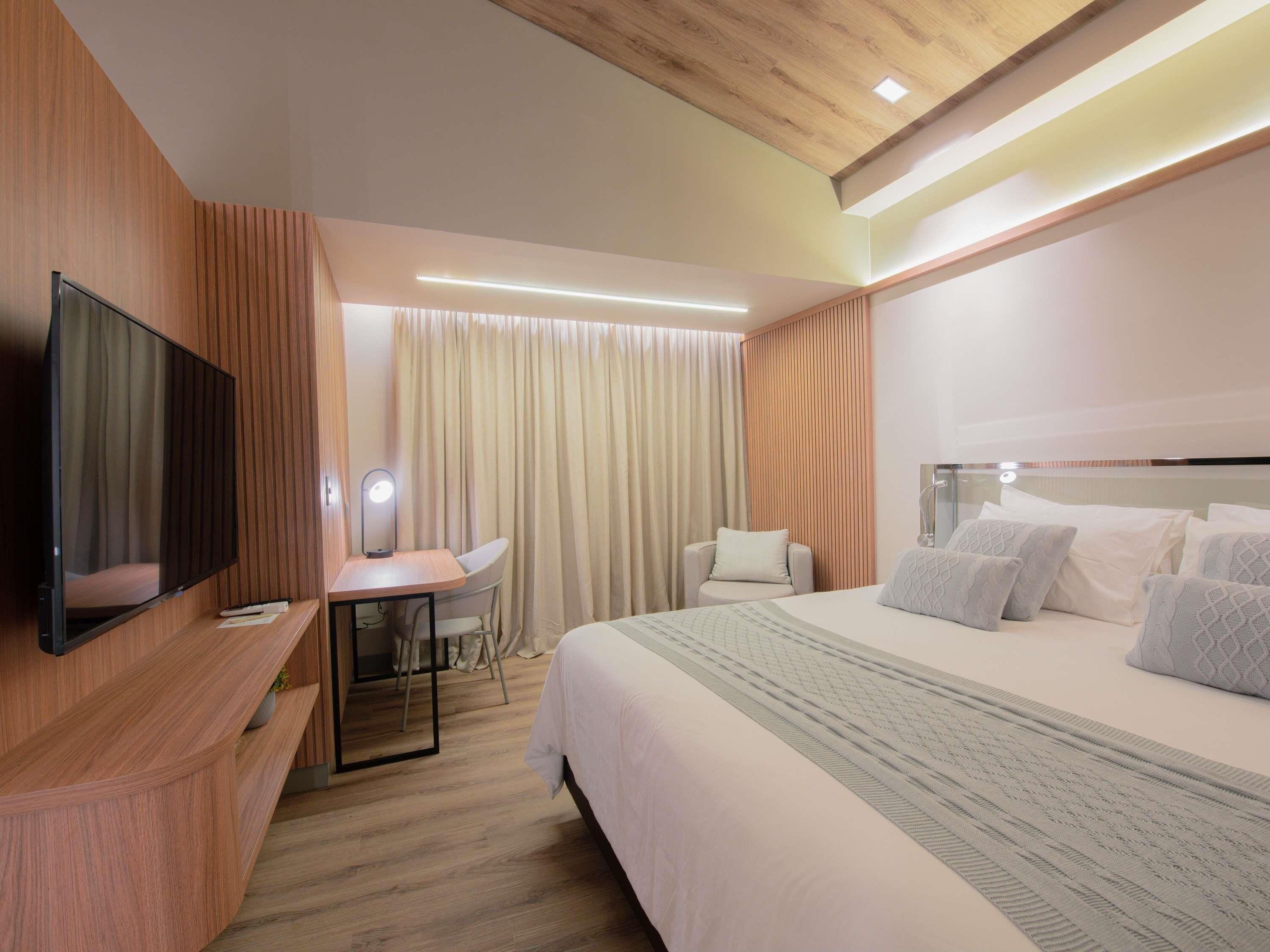 A hotel room with a bed, a desk with a chair, a television, and a mirror.