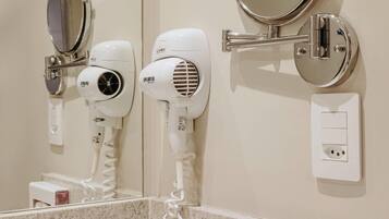 A bathroom with a mirror, two hair dryers, and a power outlet.
