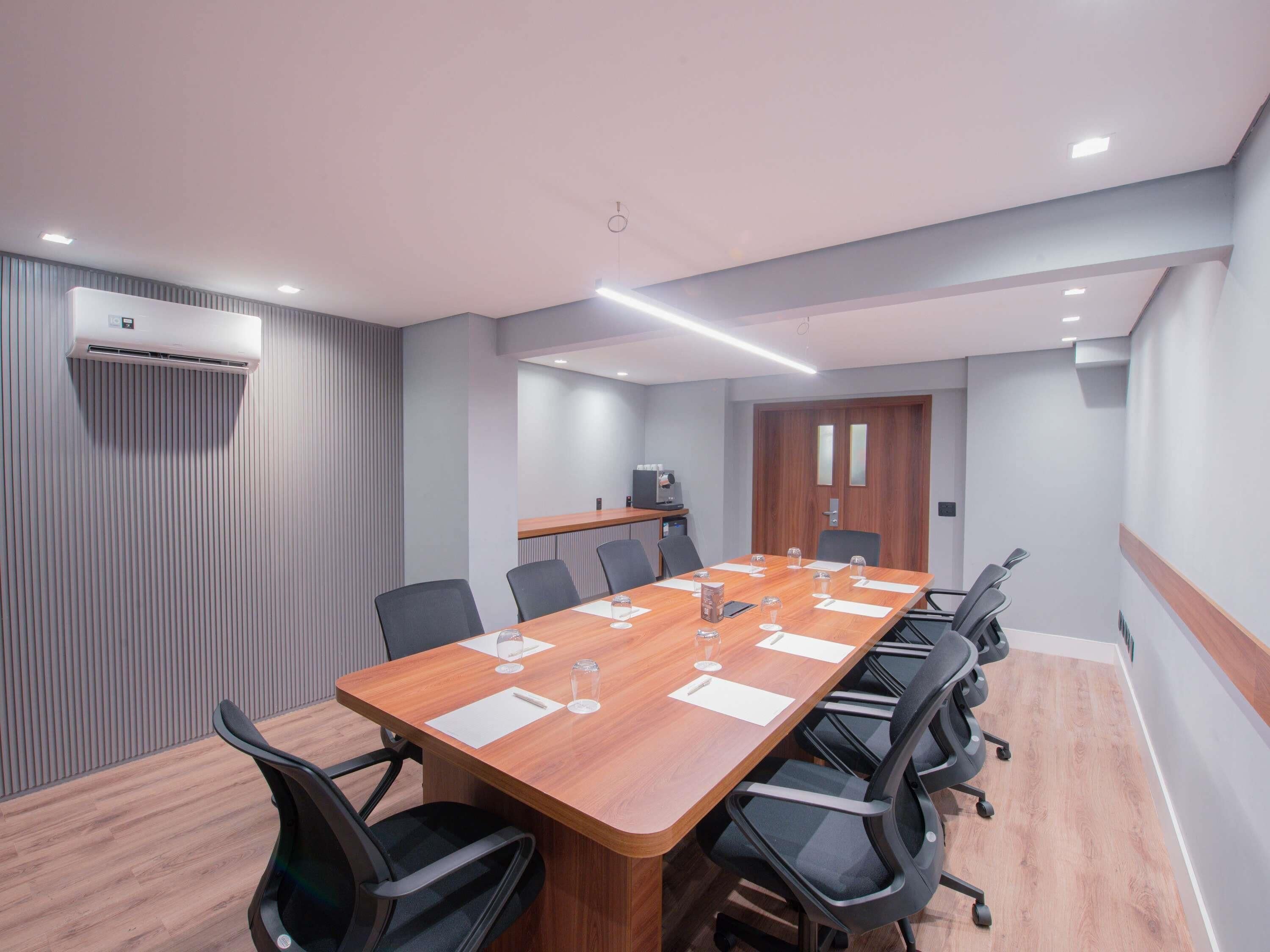 Une salle de conférence avec une longue table en bois, des chaises noires et un climatiseur fixé au mur.