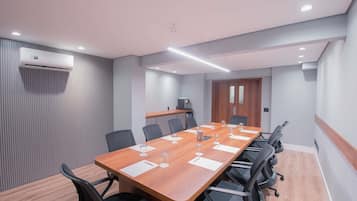 Une salle de conférence avec une longue table en bois, des chaises noires et un climatiseur fixé au mur.