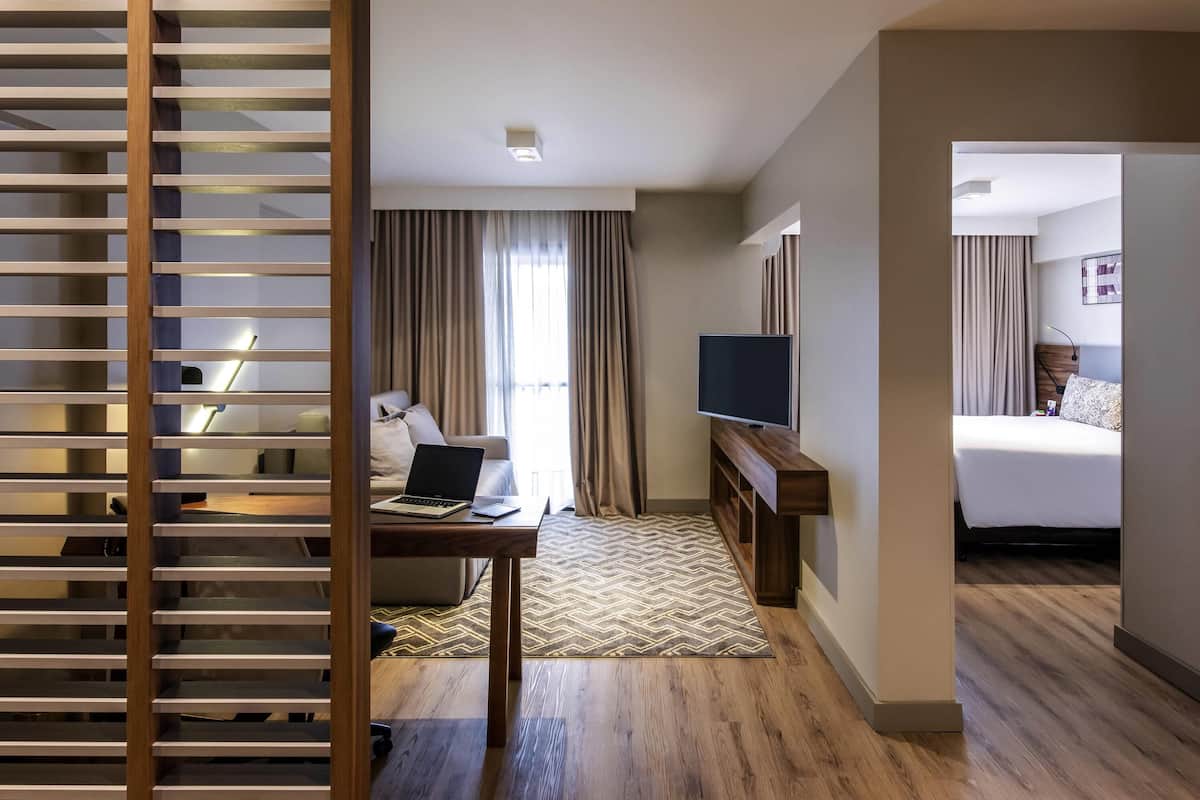 Une chambre d’hôtel avec un lit, un bureau avec un ordinateur portable, une télévision et un plancher en bois.