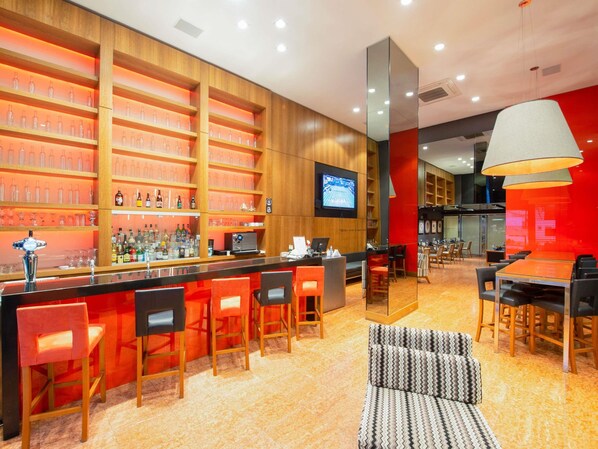 A modern bar area with wooden shelves, a flat-screen TV, and a seating area with a patterned sofa and chairs.