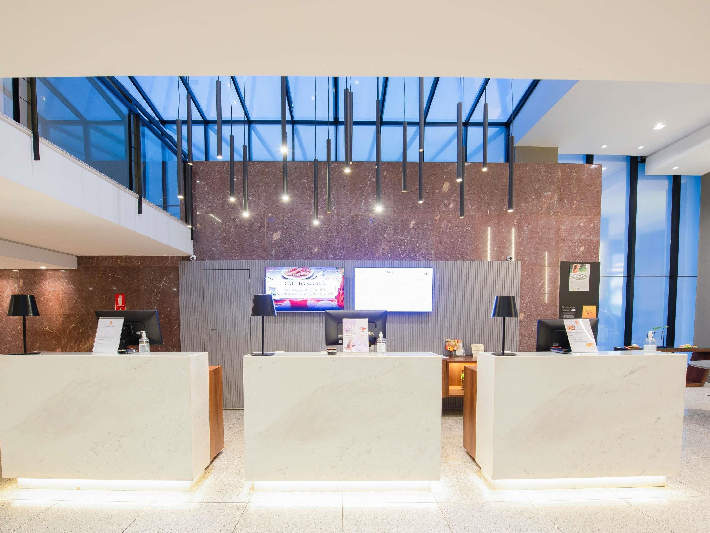 A hotel reception area with a large digital screen, marble reception desk, and a high ceiling with skylights.
