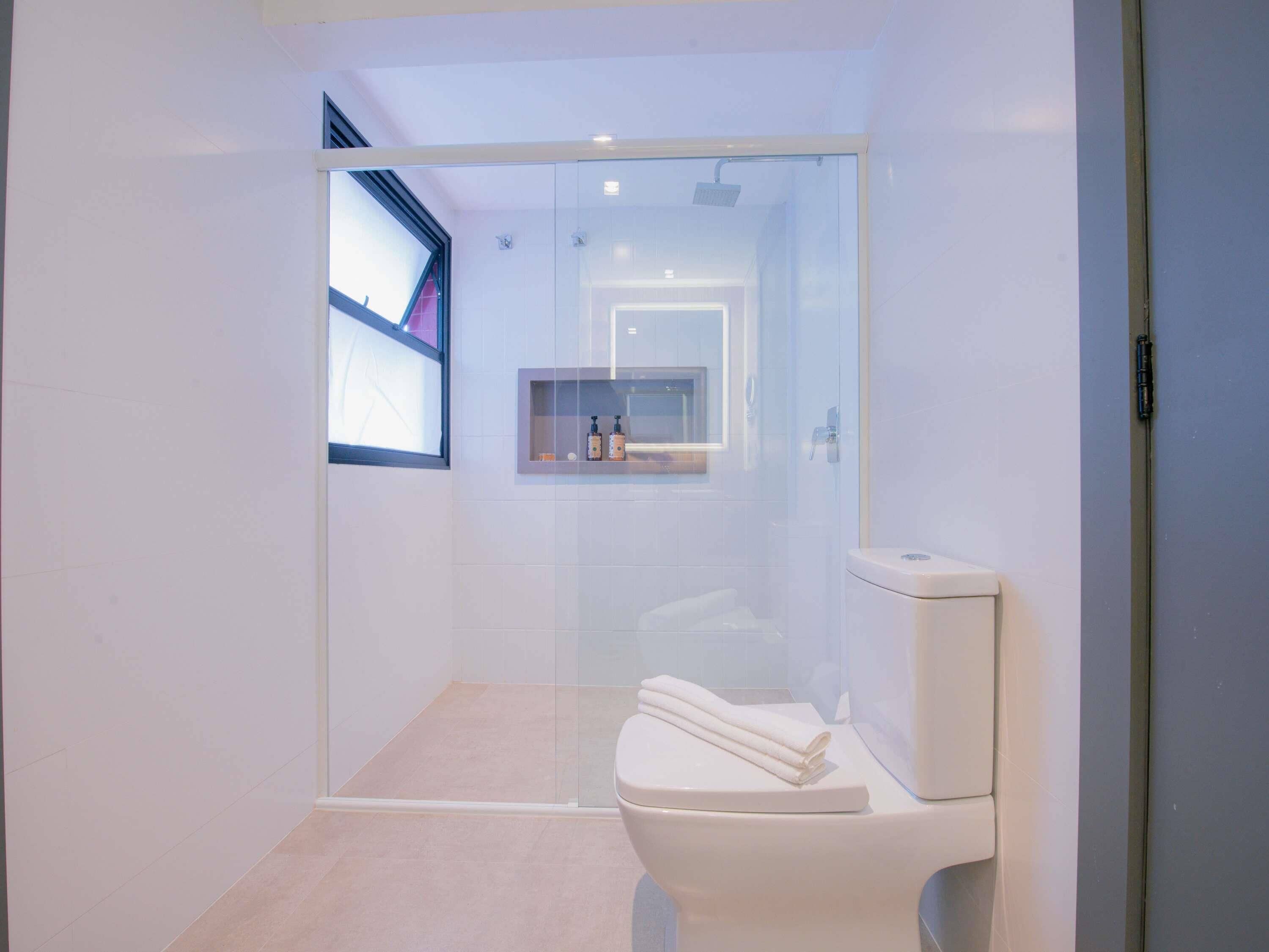 A modern bathroom with a glass shower enclosure, a toilet, and a small shelf with toiletries.