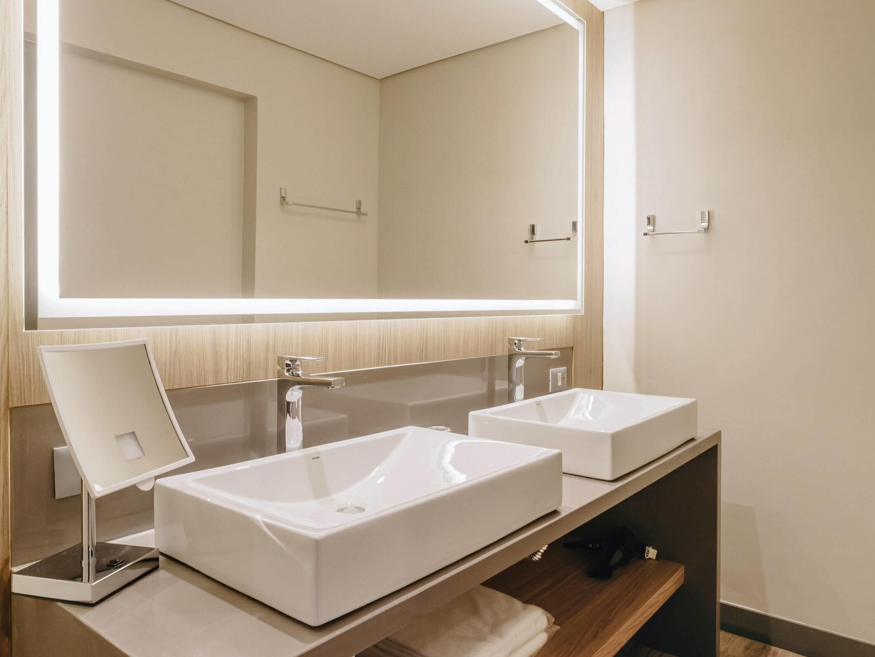 A modern bathroom with two white sinks, a large mirror, and a scale.