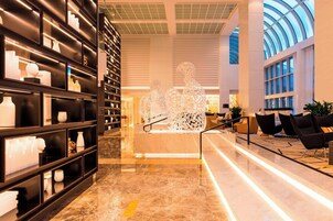A modern lobby with marble flooring, a central seating area with black chairs, and a glass ceiling.