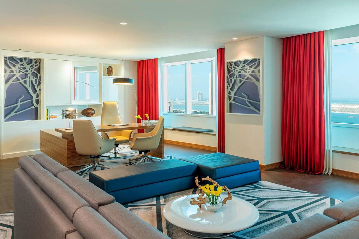 Een moderne hotelkamer met een zithoek, een bank, een bijzettafeltje en uitzicht op de skyline.