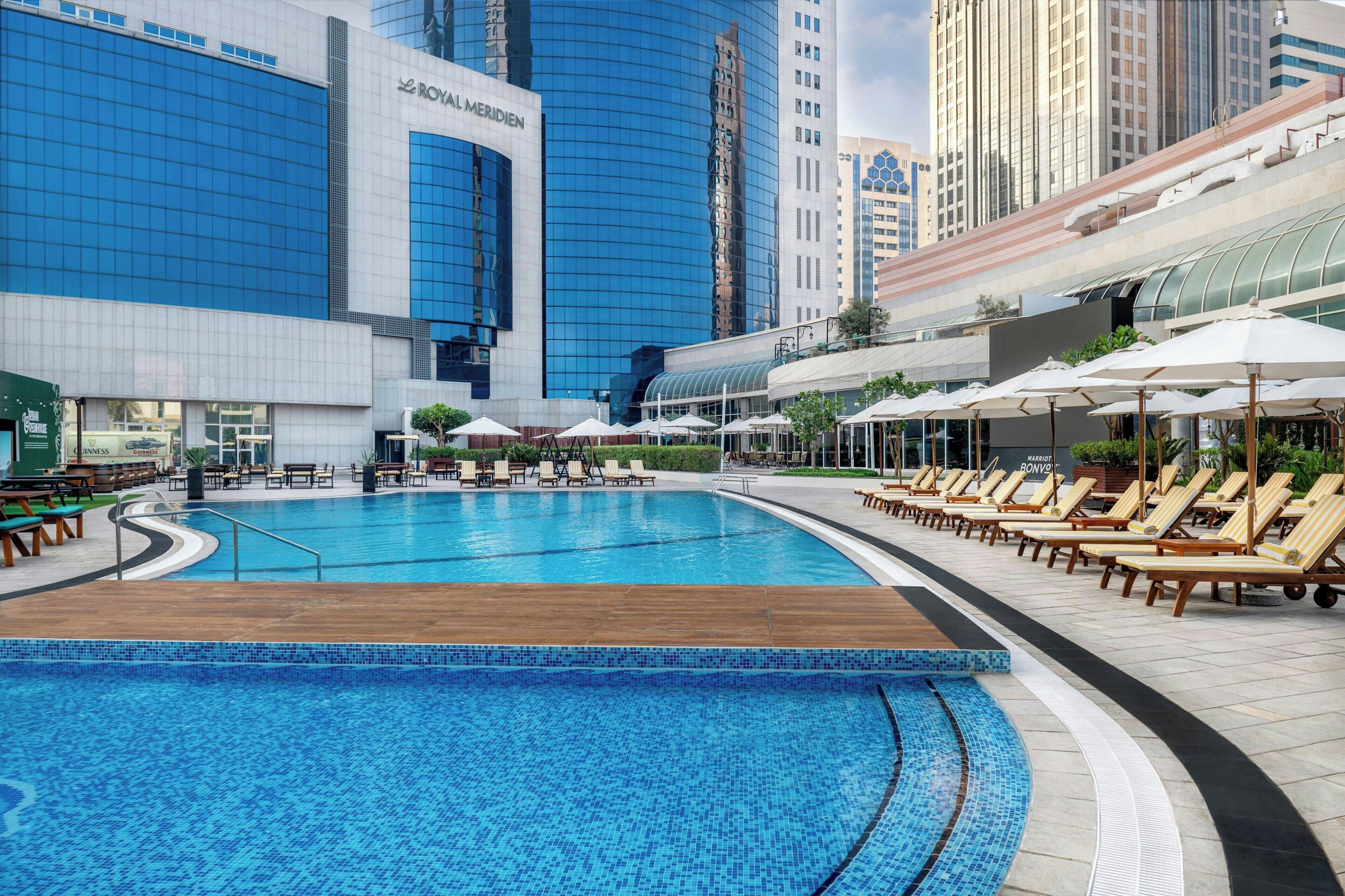 A swimming pool with lounge chairs and umbrellas, surrounded by modern buildings.