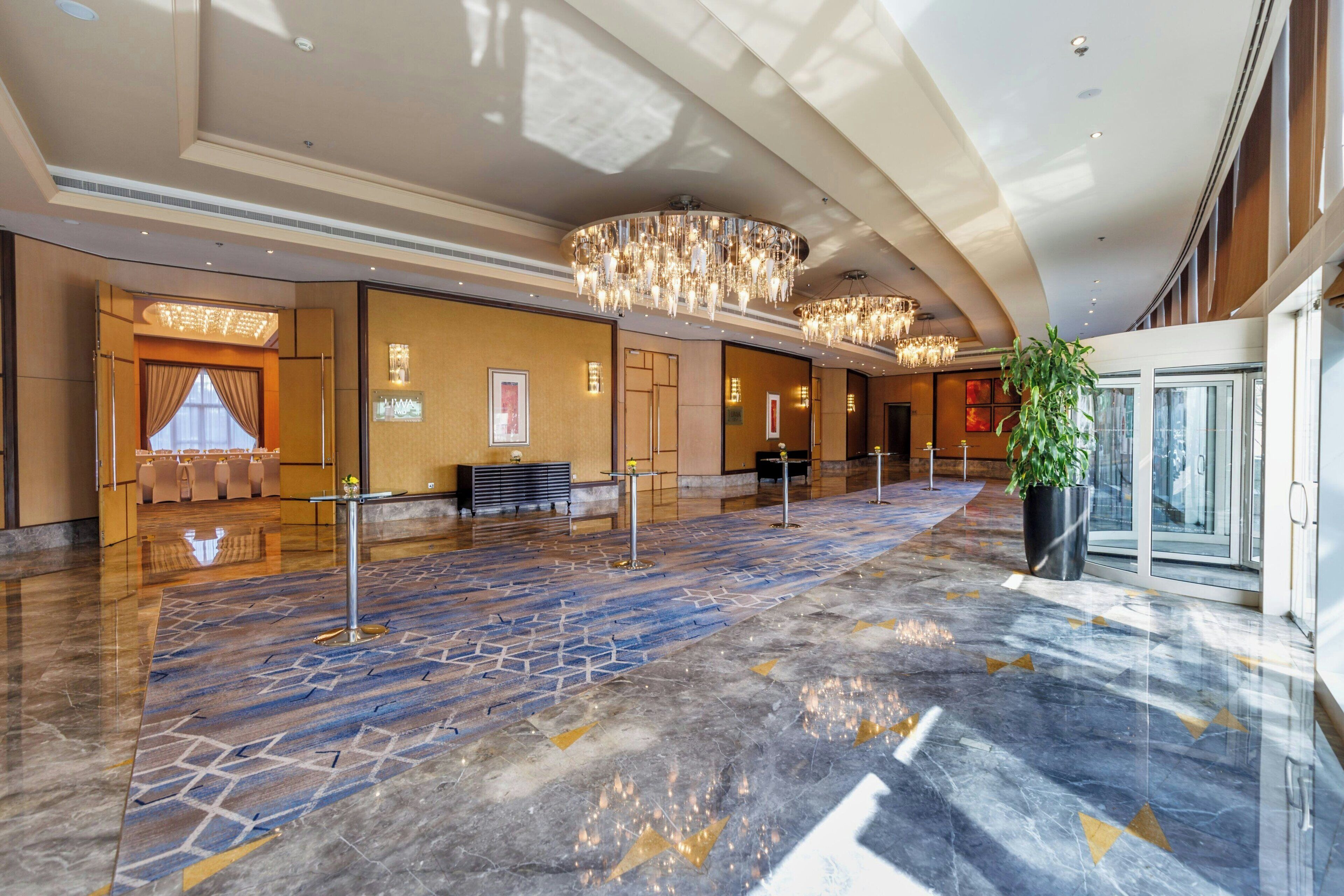 Un hall d’entrée spacieux avec un sol en marbre, un comptoir d’accueil, un espace détente et un grand lustre.