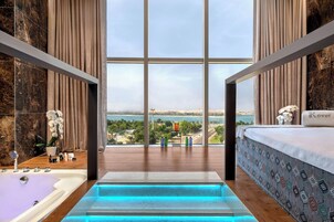 Un baño moderno con una bañera grande, cabina de ducha con mampara de vidrio y vistas a un cuerpo de agua y paisaje.