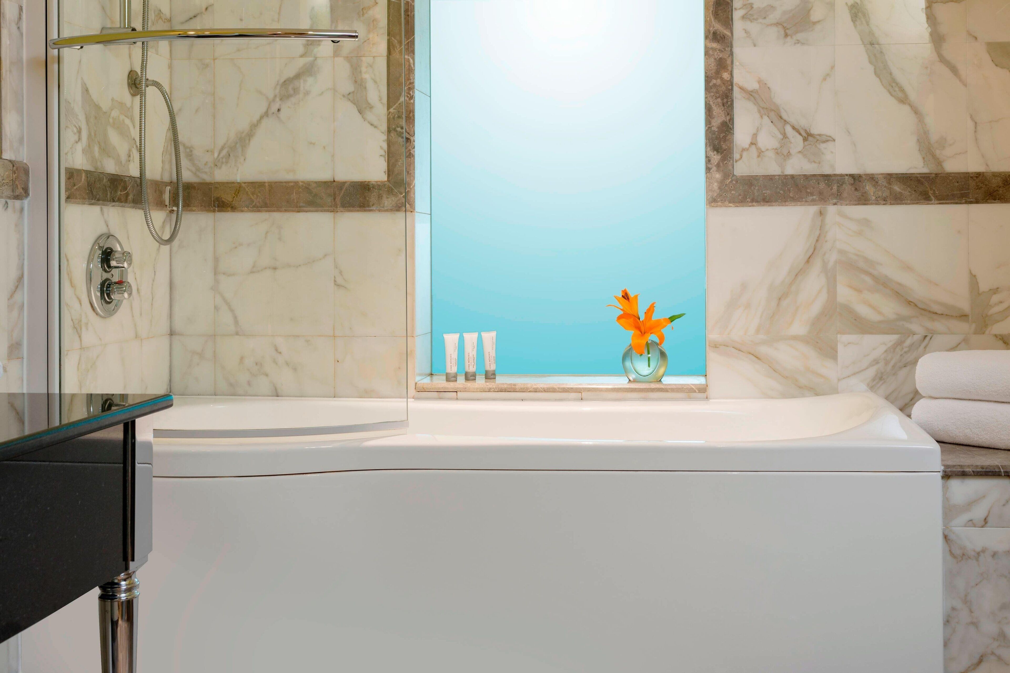 A modern bathroom with a bathtub, a glass shower enclosure, and marble walls.