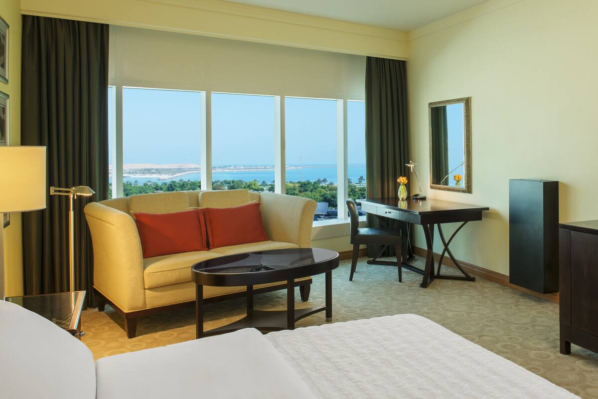 Een hotelkamer met een bed, een bank, een bureau en uitzicht op zee.