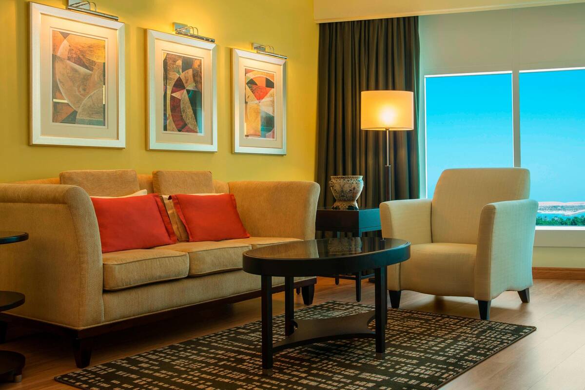 Een moderne woonkamer met een bank, fauteuil en een salontafel. Drie ingelijste kunstwerken hangen aan de muur en een lamp staat naast de bank.