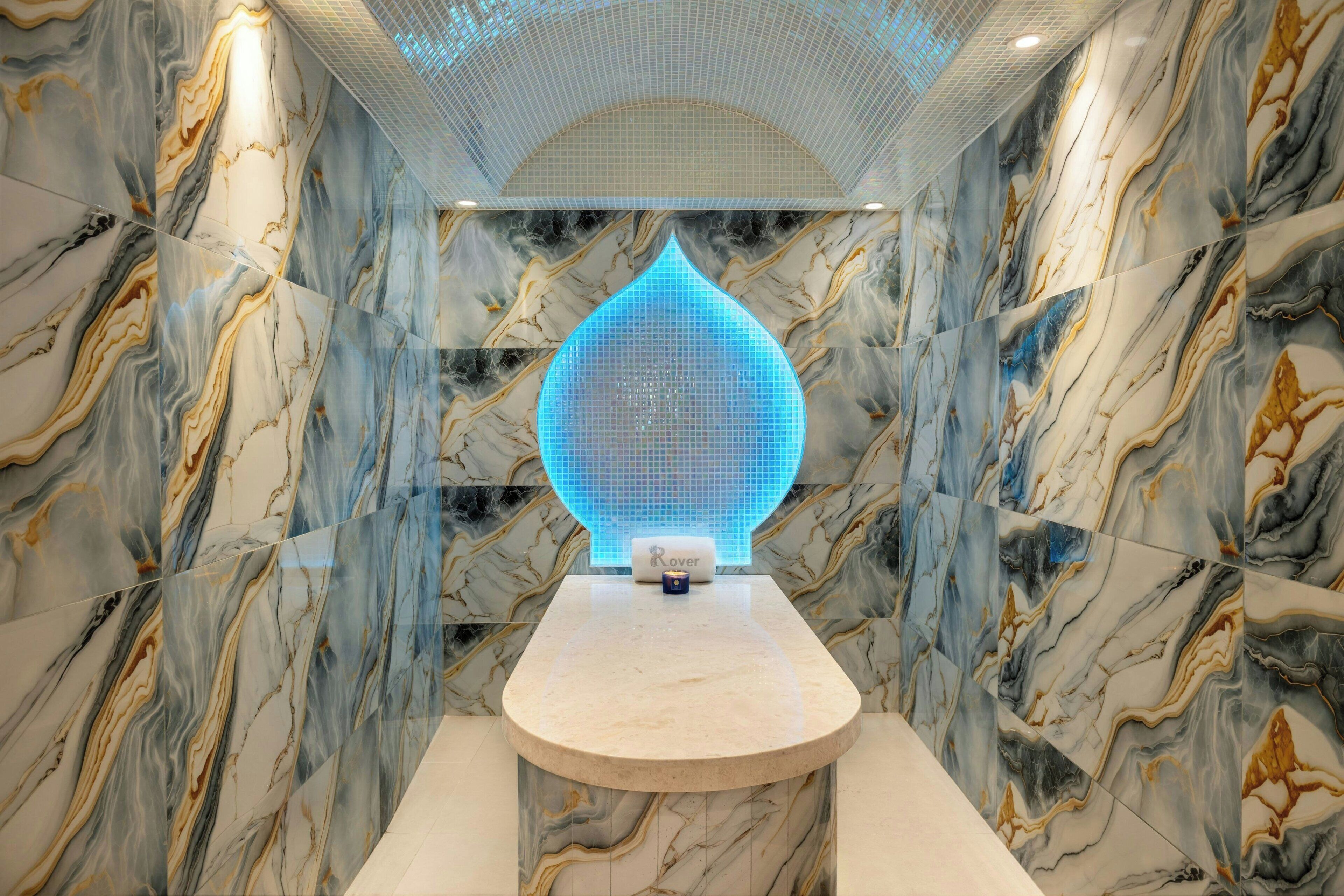 Een spa ruimte met een marmeren wand, een blauw lichteffect en een klein tafeltje met een fles.