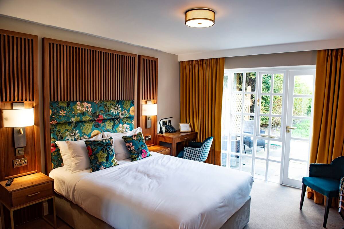 Habitación de hotel con una cama grande, un escritorio y una silla. Hay una ventana con cortinas y vistas a zonas verdes.