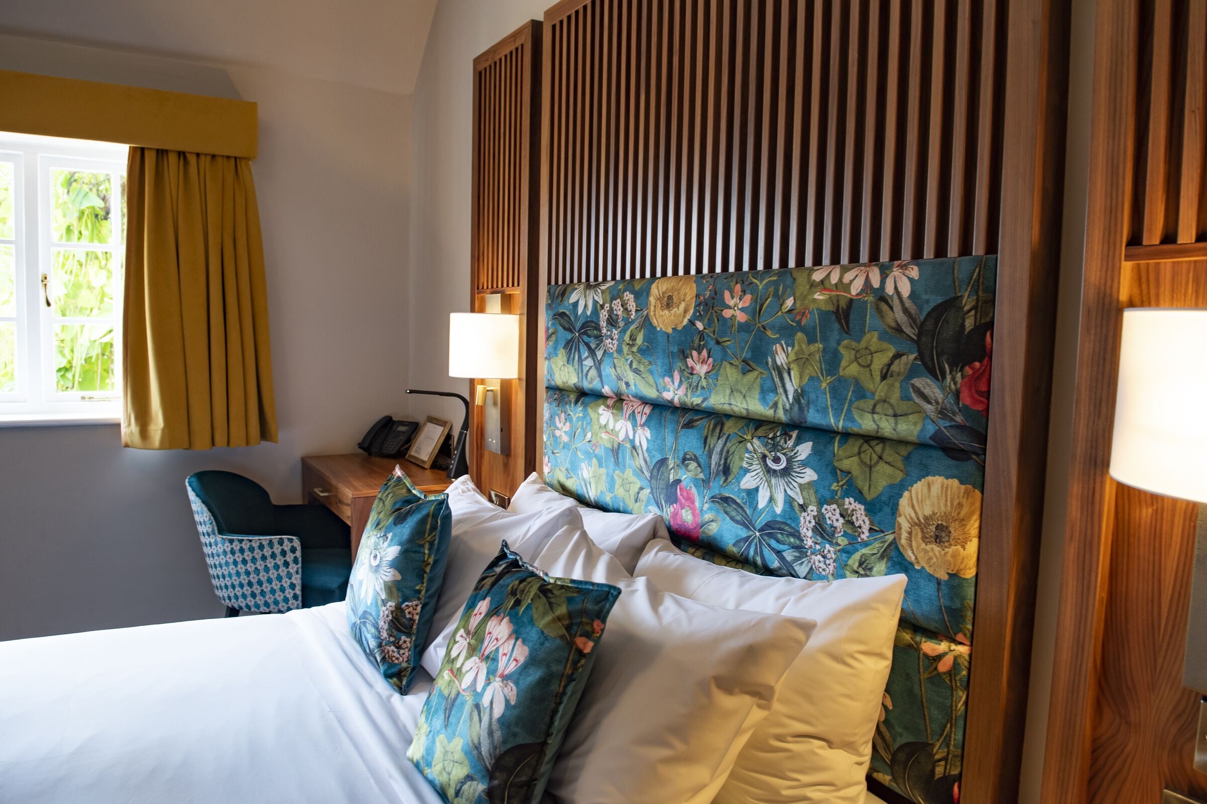 A hotel room with a bed, a desk with a lamp, a chair, and a window with curtains.