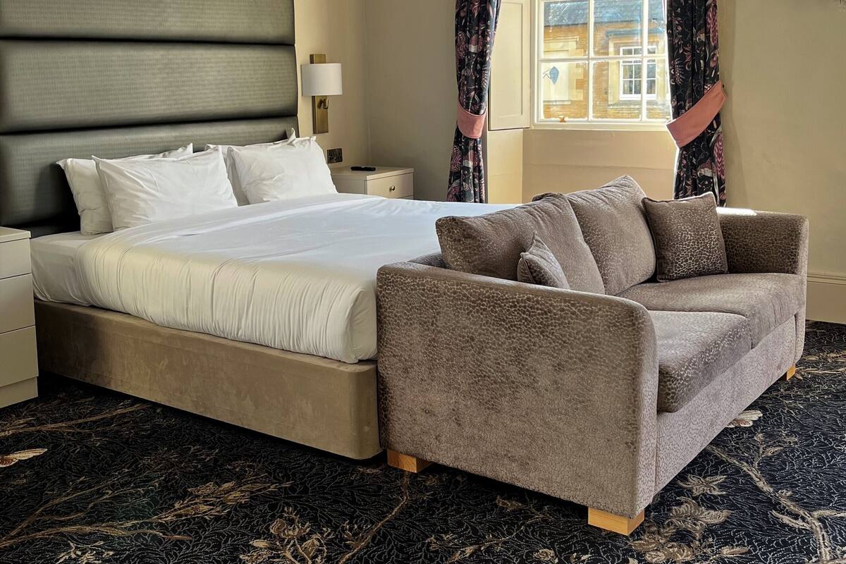 Un dormitorio con una cama grande, un sofá, una mesita de noche y una ventana con cortinas.