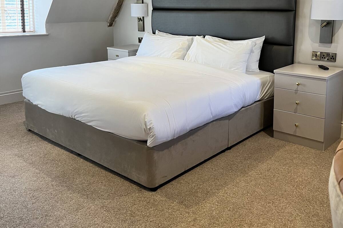Un dormitorio moderno con una cama grande, una mesita de noche, una lámpara y una ventana con persianas.