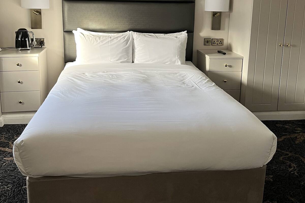 Una habitación de hotel con una cama grande, dos mesitas de noche, un armario y una lámpara en el techo.