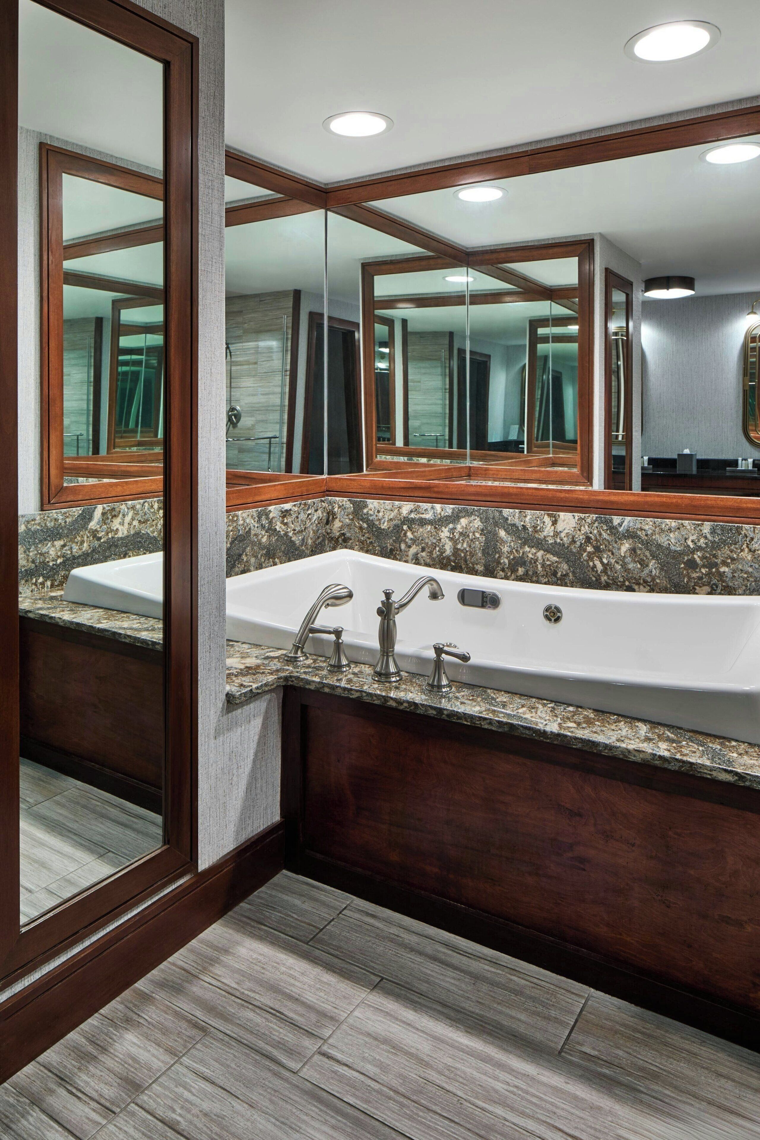A bathroom with a large mirror, a freestanding bathtub, and a granite countertop.