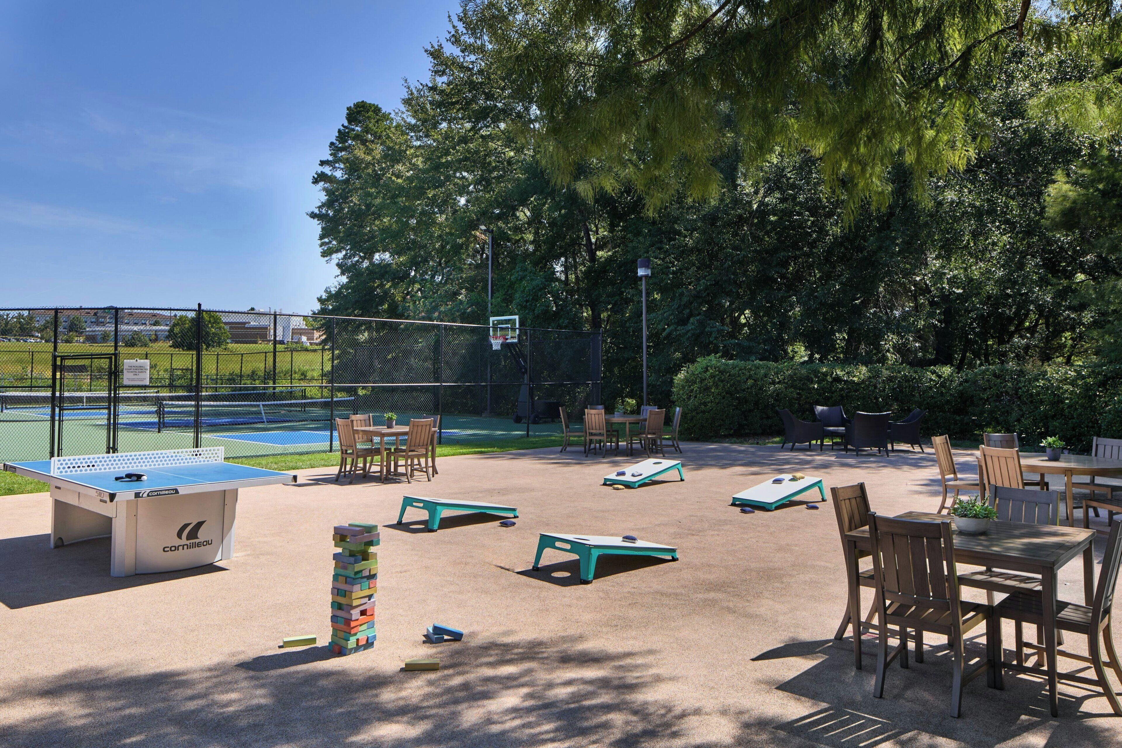 An outdoor recreational area with a foosball table, shuffleboard table, and a tennis court.