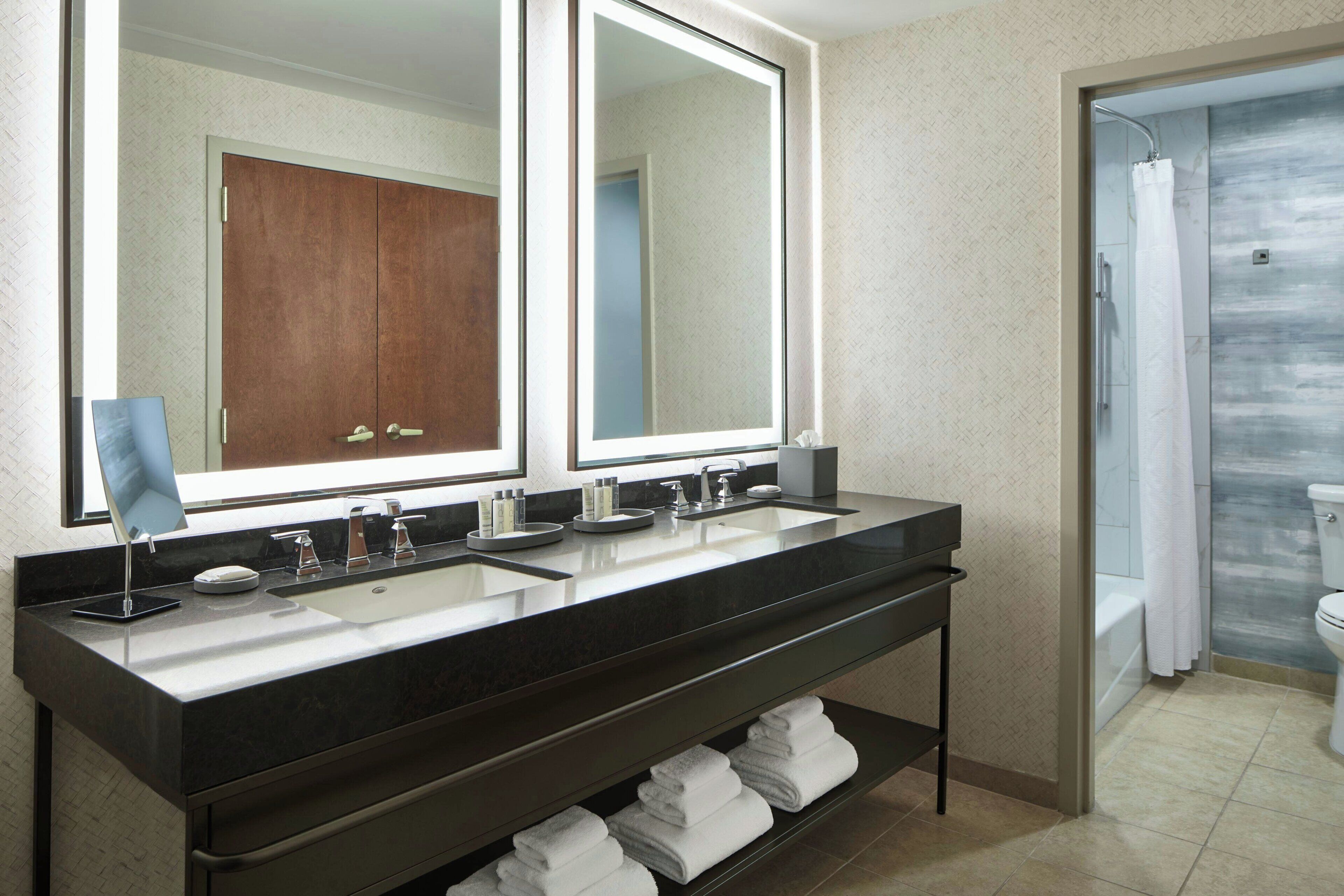 A modern bathroom with a double sink vanity, a large mirror, and a shower area.