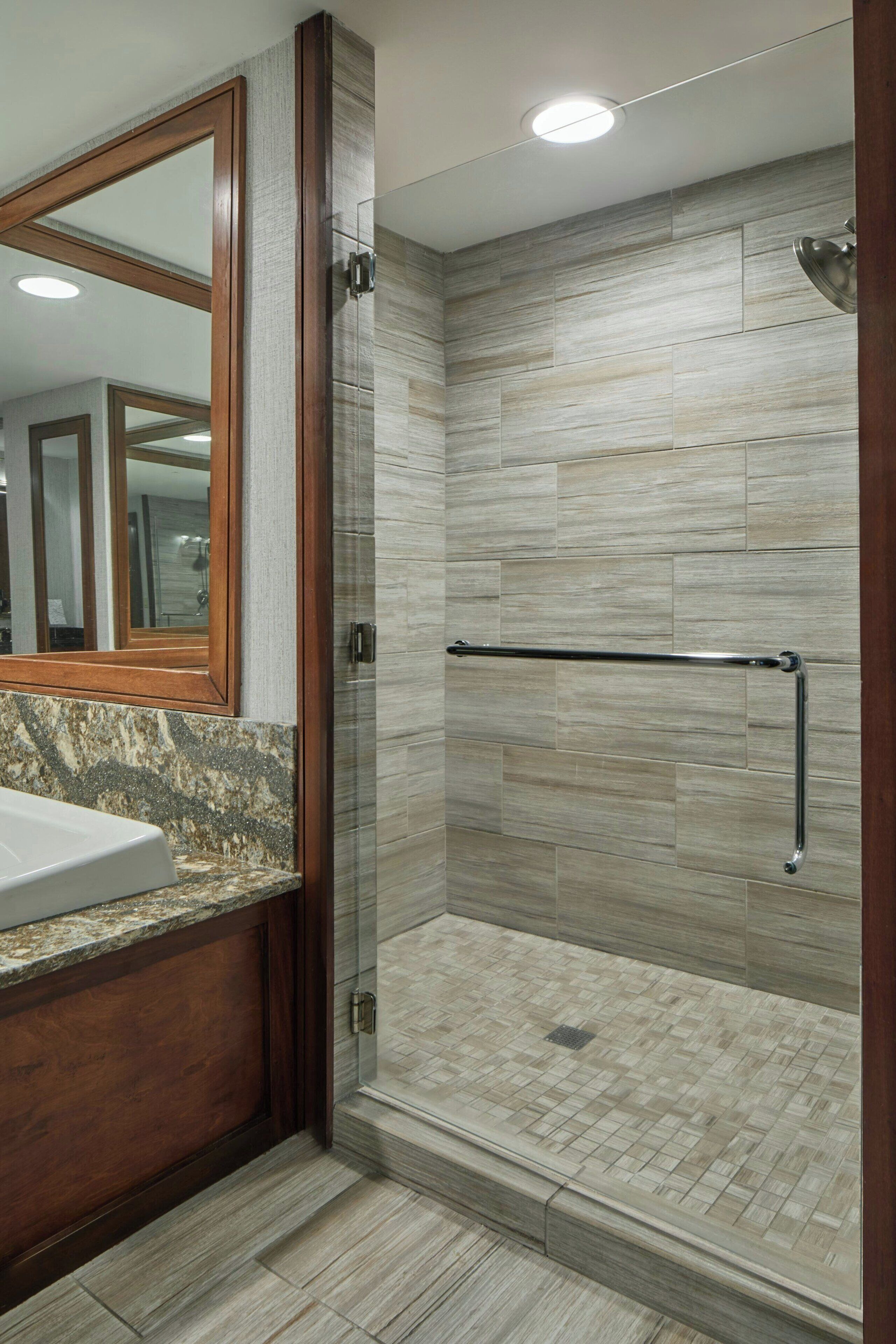 Un baño moderno con cabina de ducha de vidrio, tocador de madera y un espejo grande.