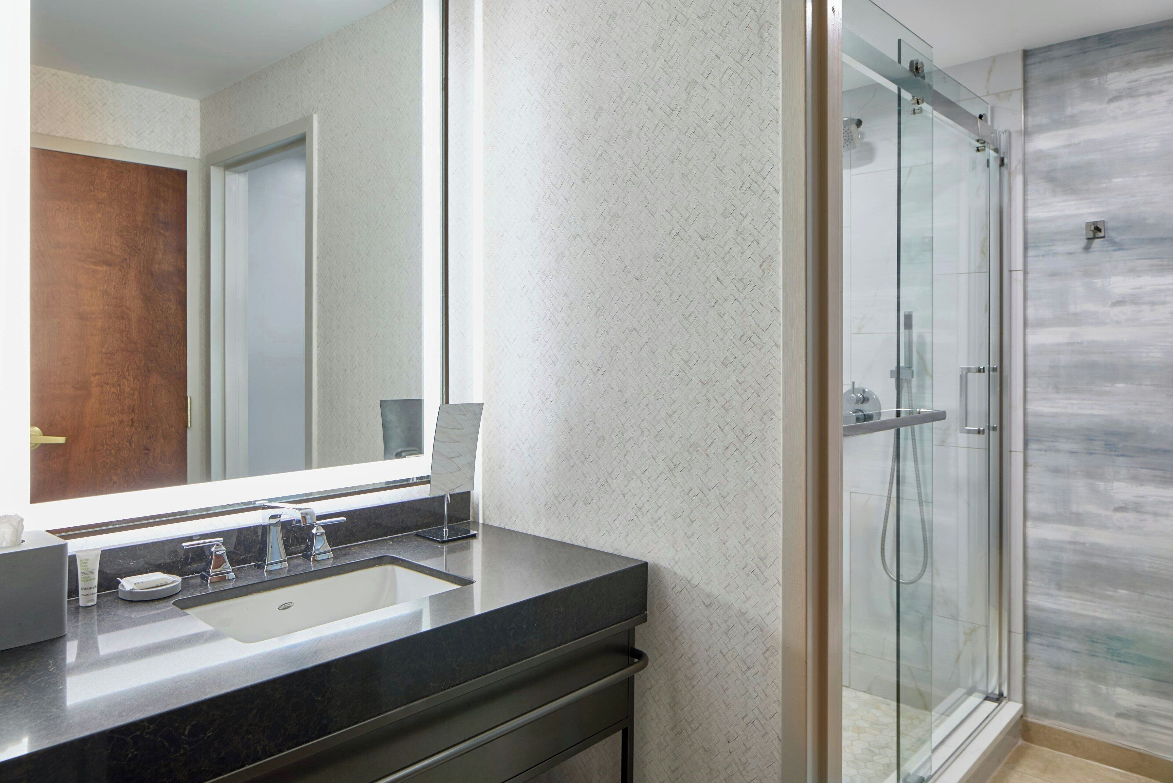 Un baño moderno con un espejo grande, un lavamanos y una ducha con paredes de vidrio.