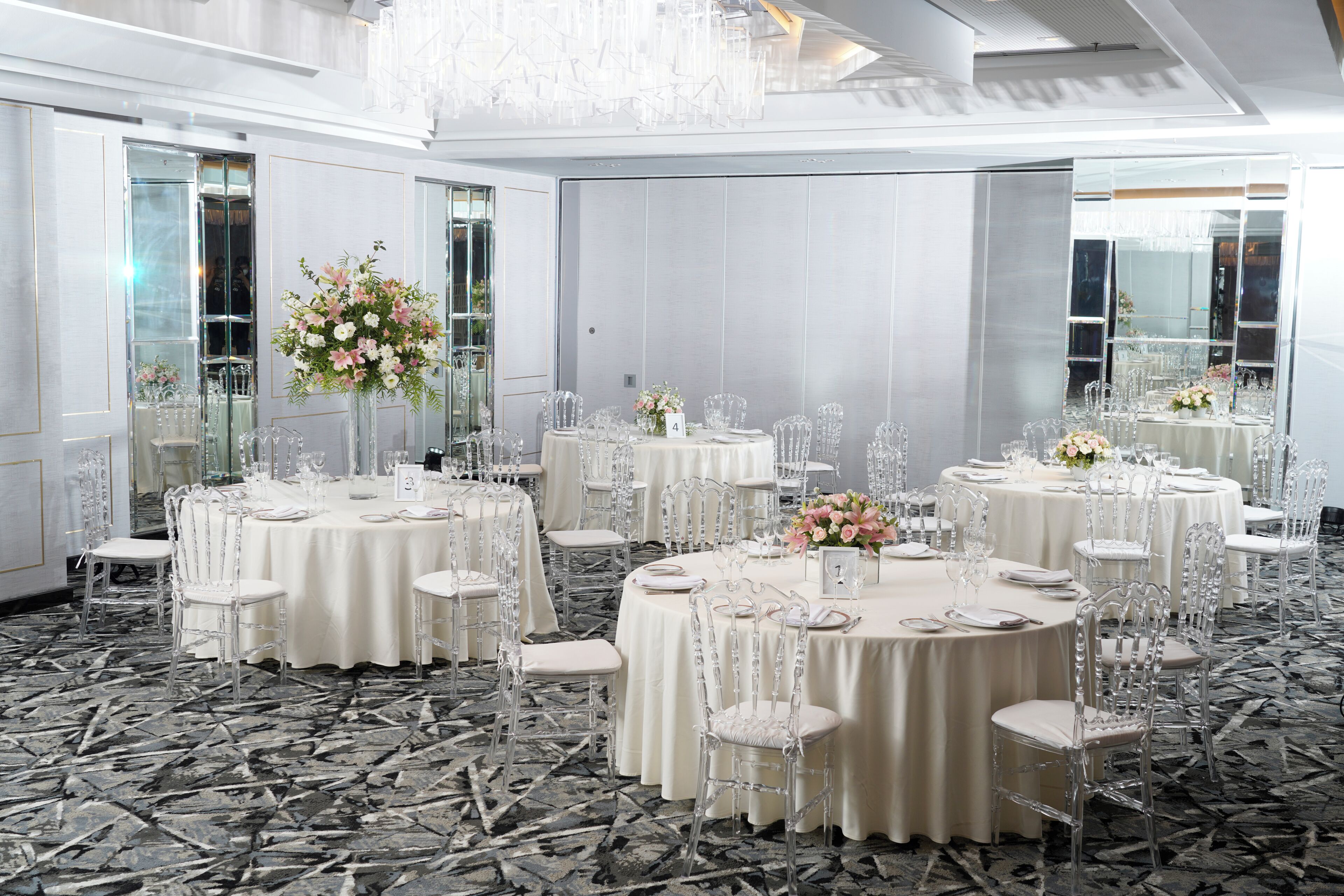 Un salón de banquetes con mesas redondas, sillas transparentes y centros de mesa florales.